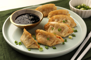 Delicious gyoza (asian dumplings) with green onions, soy sauce and chopsticks on table, closeup