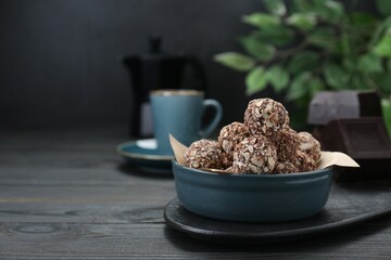 Bowl of delicious sweet chocolate candies on black wooden table, space for text
