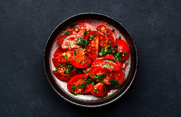 Simple vegan tomato salad with parsley, garlic, jalapeno and olive oil dressing, black table background, top view
