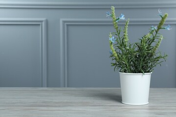 Beautiful artificial plant in flower pot on white wooden table near grey wall, space for text