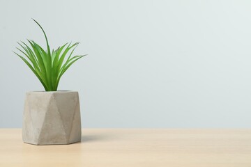 Beautiful artificial plant in flower pot on wooden table against light grey background, space for text
