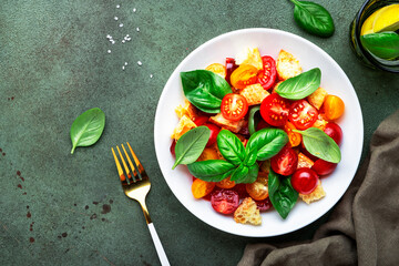 Panzanella summer vegetable salad with stale bread, colorful tomatoes, olive oil, salt and green basil, green table background, top view