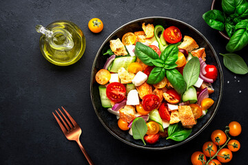 Panzanella salad with stale bread, colorful tomatoes, mozzarella cheese, onion, olive oil, salt and green basil, black table background, top view