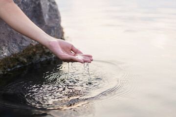 Man's hand touching water in the midst of nature