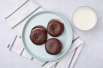 Tasty sweet choco pies and glass of milk on light gray table, flat lay