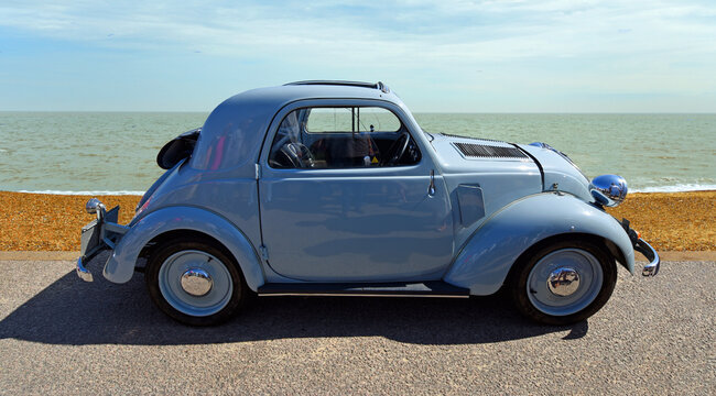 Classic Fiat 500 parked on seafront promenade beach and sea in background.