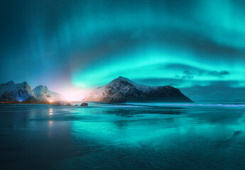 Northern Lights and beach at starry night in winter. Lofoten islands, Norway. Beautiful Aurora borealis. Sky with polar lights. Landscape with aurora, sea with sky reflection in water, mountains