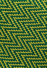 Knitted texture with chevron pattern. Texture of overlay mosaic fabric with yellow green geometric ethnic pattern.