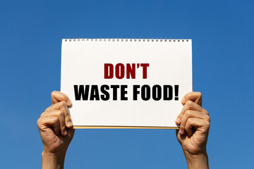 Don't waste food text on notebook paper held by 2 hands with isolated blue sky background. This message can be used as business concept about don't waste food.