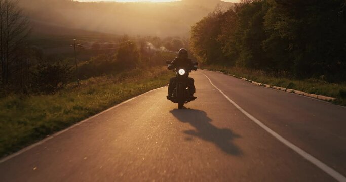 A man driving a motorbike through an empty highway during beautiful sundown.