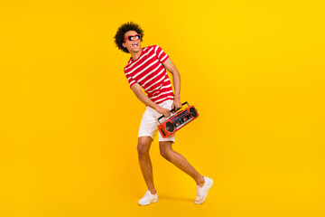 Fototapeta na wymiar Full size photo funky guy dance youth party carry boom box wear shirt pants shoes sun specs isolated yellow color background