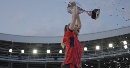 Portrait of Caucasian female soccer football player celebrating victory in the championship, lifting the trophy above her head in a huge stadium