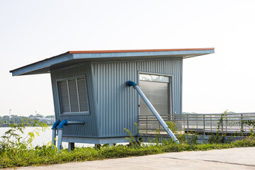 A low angle view through the grass to a blue zinc hut with water pipes.