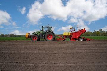 Seitliche Ansicht einer modernen roten Kartoffellegemaschine mit grünen Traktor, beim Kartoffel legen im Frühjahr.