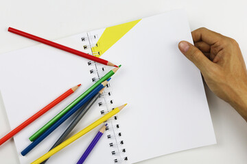 notebook with colored pencils and hand on white background