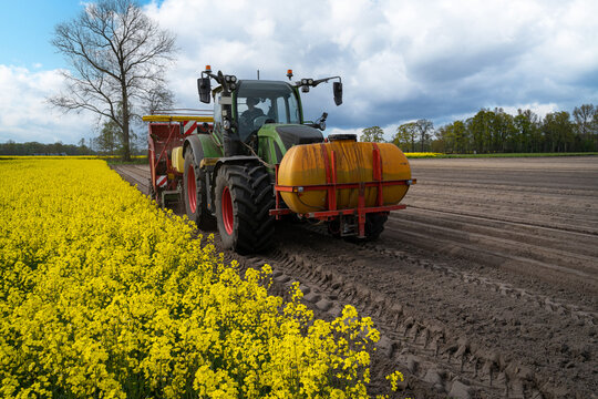Moderner Traktor mit einem frontseitig montierten Flüssigkeitsbehälter und angehängtem Kartoffel-Legegerät im Frühjahr auf einem Kartoffelfeld im Einsatz. 