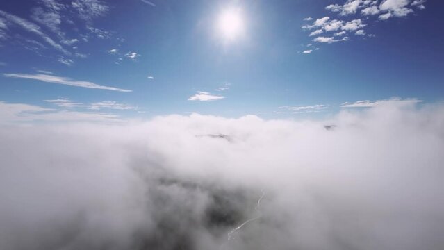 We fly through the clouds. Blue sky with clouds and sun. 4K video of flying in the clouds on a sunny day with a view of the road through the clouds