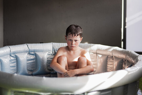 Cute kid with depressed face sitting in inflatable pool
