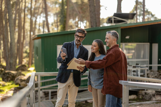 Real estate agent showing mature couple smartphone on sustainable property