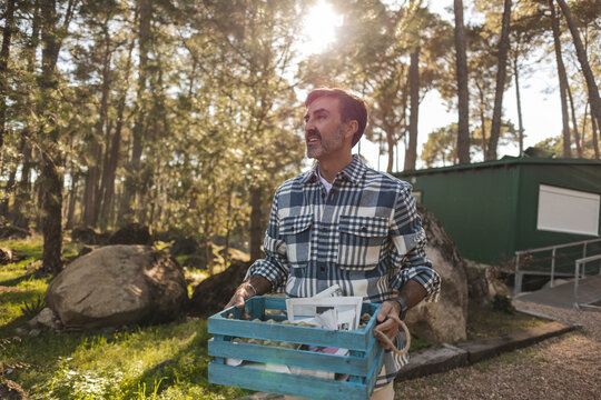 Mature man carrying crate with separated waste in garden