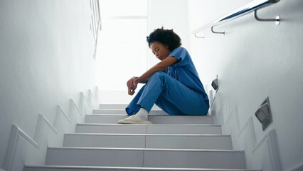 Stressed and tired female nurse wearing scrubs sitting on hospital stairs - shot in slow motion