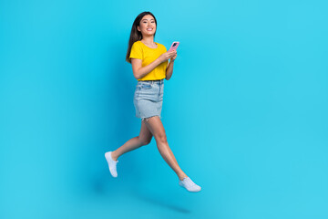 Fototapeta na wymiar Full size portrait of charming energetic girl jumping use smart phone blogging isolated on blue color background