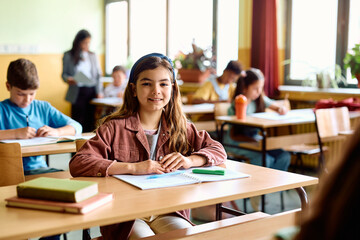 Happy schoolgirl during class in classroom looking at camera.