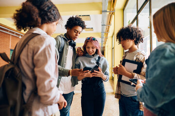 Black high school student showing to his classmates something on his cell phone in hallway. - obrazy, fototapety, plakaty