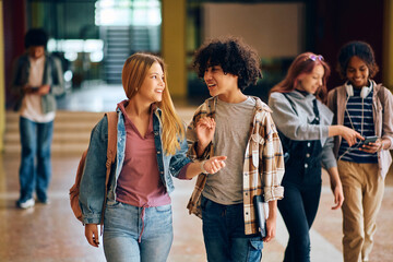 Happy high school friends talk while walking through hallway.