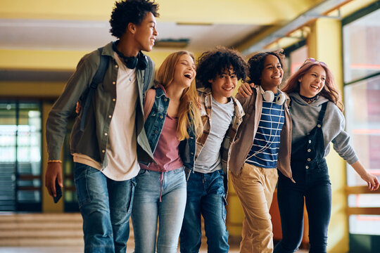 Multiracial Group Of Cheerful High School Friends Walk Through Hallway At School.