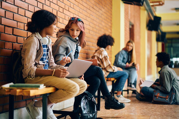 Teenage girls studying together in hallway at high school.