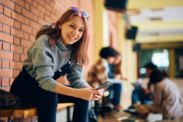 Happy high school student text messaging on cell phone and looking at camera. - obrazy, fototapety, plakaty