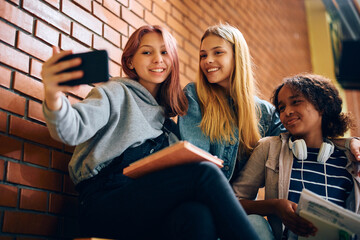 Happy teenage girls taking selfie with cell phone at high school.