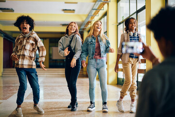 Obraz premium Cheerful high school students goof around while friend is filming them with phone.