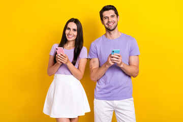 Naklejka premium Portrait of positive partners hold use smart phone chatting eshopping isolated on yellow color background
