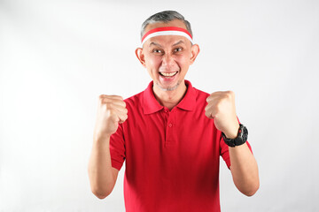 Portrait of Asian Man wearing red and white Indonesia flag attribute clenched and excited...