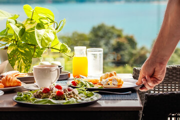 Waiter serving table with drinks and food in restaurant in luxury resort with sea view. Closeup of...