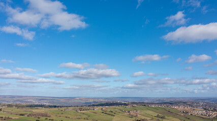 Aerial drone photo of the beautiful town of Thornton in Bradford in the UK showing the farmers fields in the Spring time on a hot sunny day with clouds in the sky.
