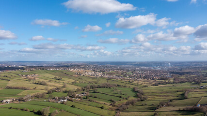 Fototapeta premium Aerial drone photo of the beautiful town of Thornton in Bradford in the UK showing the farmers fields in the Spring time on a hot sunny day with clouds in the sky.