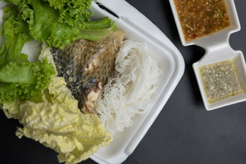 Grilled fish served with fresh vegetable, noodle and spicy sauce on a black background.