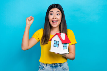 Photo of young crazy japanese woman fist up hooray wear yellow t-shirt celebration bought new apartments isolated on blue color background