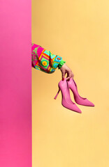 Creative scene sustainable fashion pink high heels shoes in a womans's hand. Colorful sleeve of a dress on a pink and yellow background.