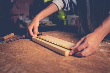 Female use tape measure to assemble wooden pieces. Professional carpenter at work measuring wooden planks.