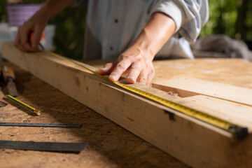 Female use tape measure to assemble wooden pieces. Professional carpenter at work measuring wooden planks.