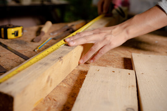 Female use tape measure to assemble wooden pieces. Professional carpenter at work measuring wooden planks.