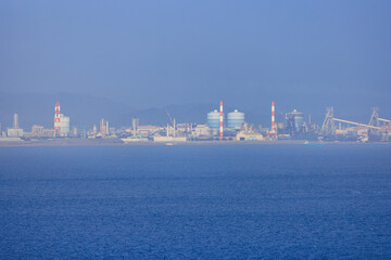 Red and white chimneys at industrial plant on coast in hazy atmosphere