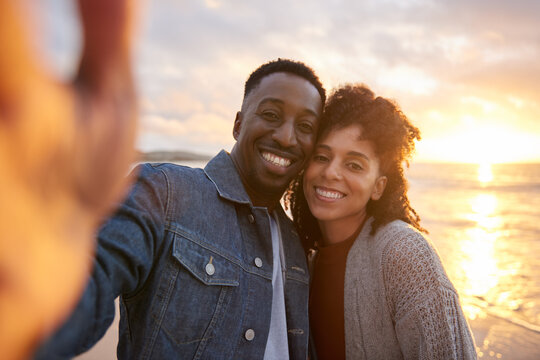 Smiling young multiethnic couple taking selfies on a beach at sunset
