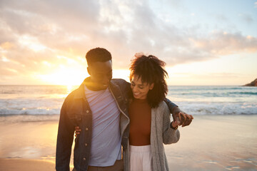 Smiling multiethnic couple walking arm in arm on a beach at sunset