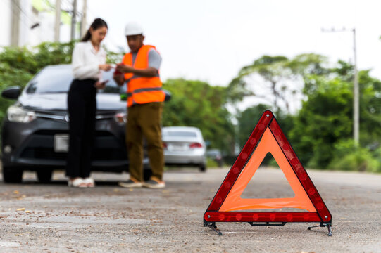 Close up red emergency triangle warning sign on road with blurred woman and rescue man background 