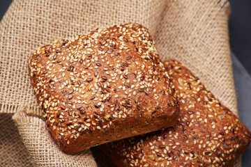 Two freshly baked rustic square shaped bread buns with sesame seeds extremely close up on the vintage rustic country style sackcloth - Powered by Adobe